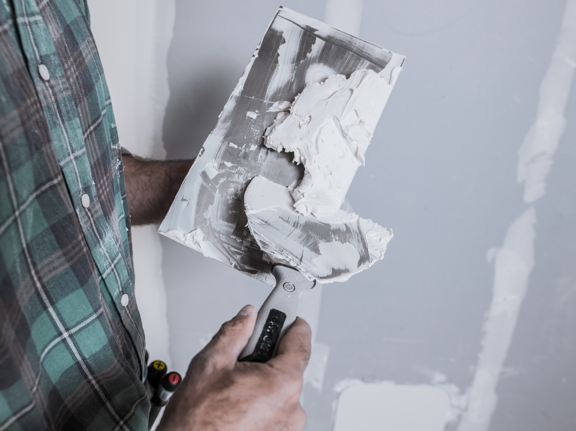 A mason prepares the putty with trowels to apply it to the plasterboard.